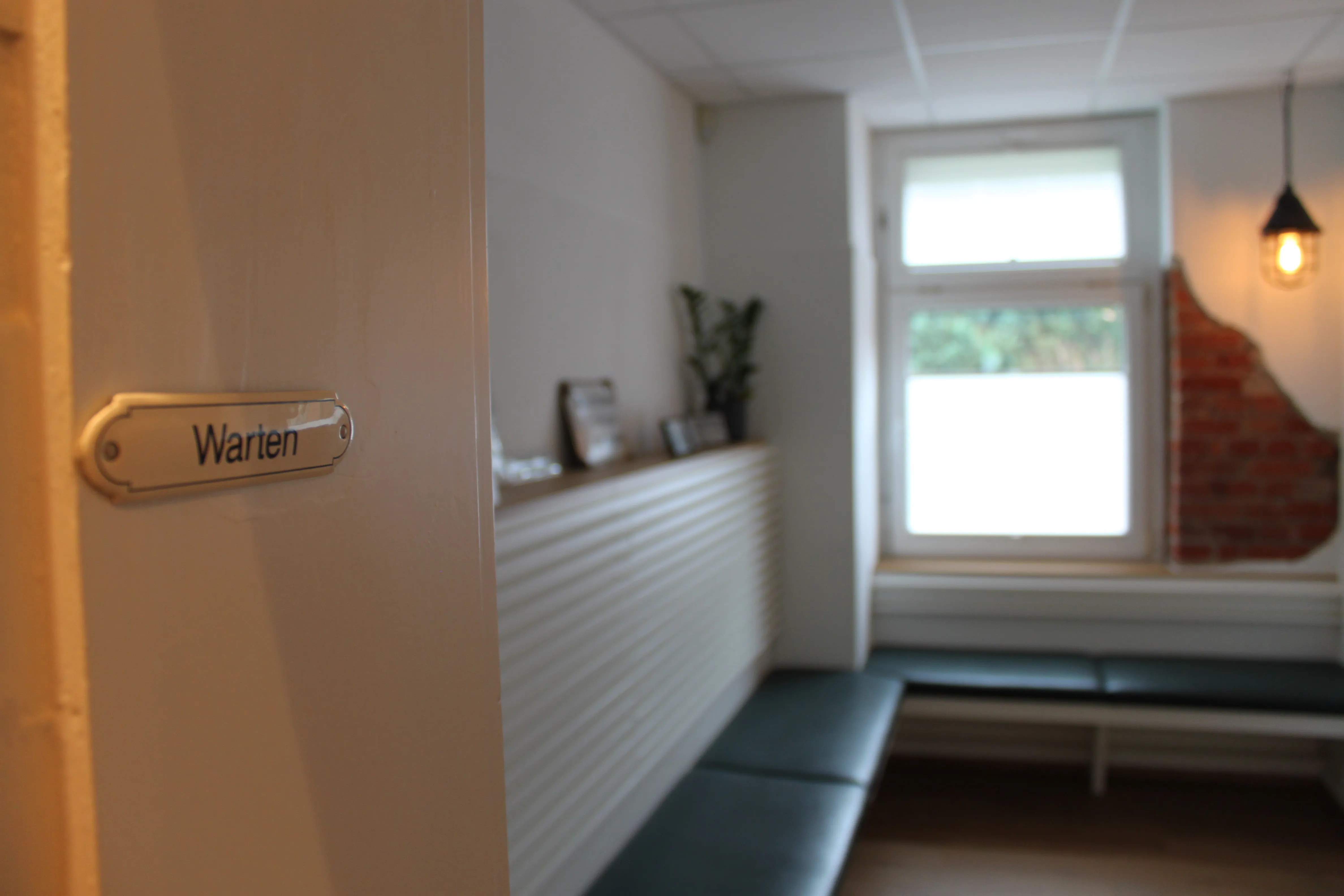 Türschild Warten, dahinter das Wartezimmer der Praxis